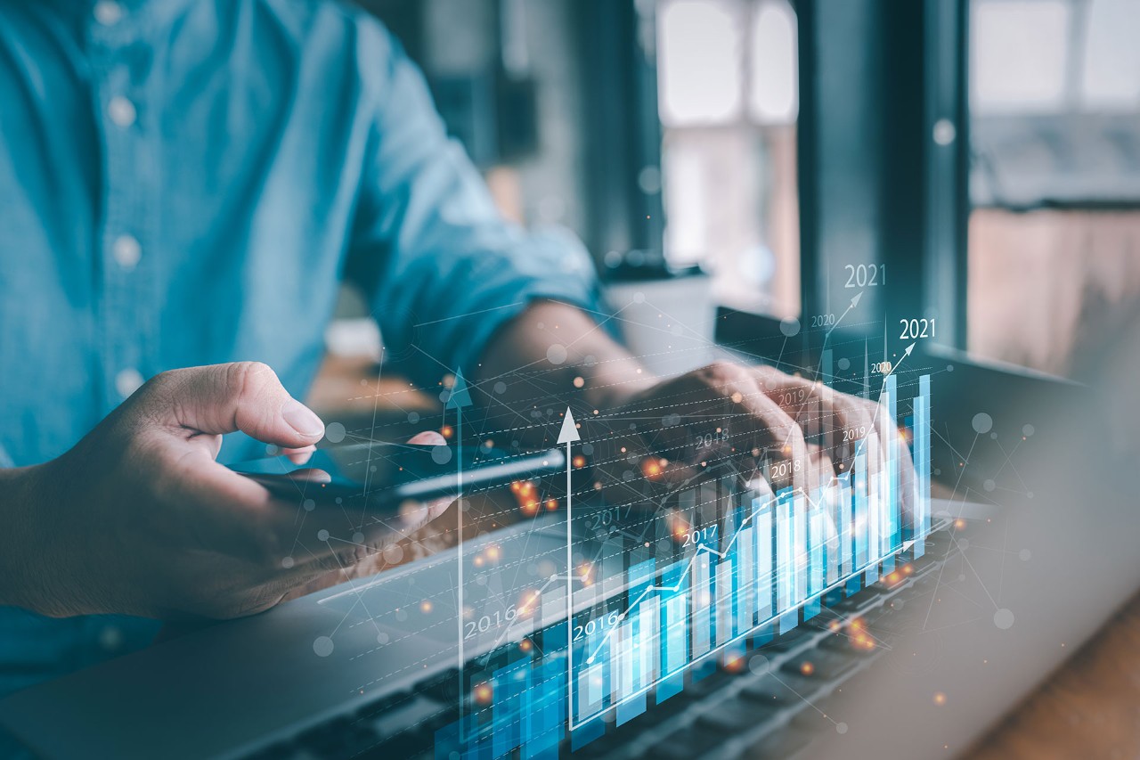 person using smartphone and laptop with financial graphs overlay, symbolizing fintech and data analytics